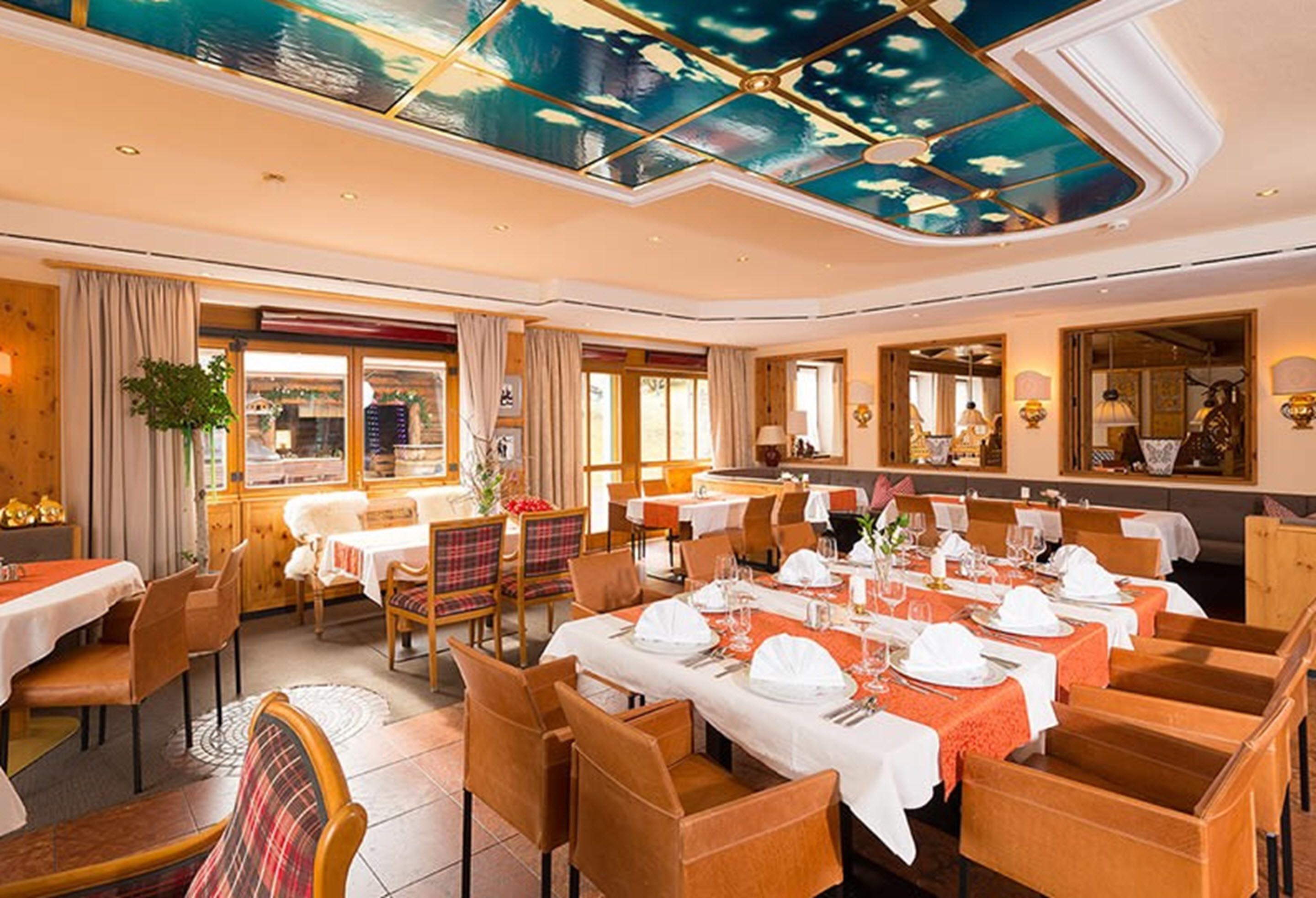 A restaurant with multiple tables set for dining, featuring a ceiling with a painted sky design.