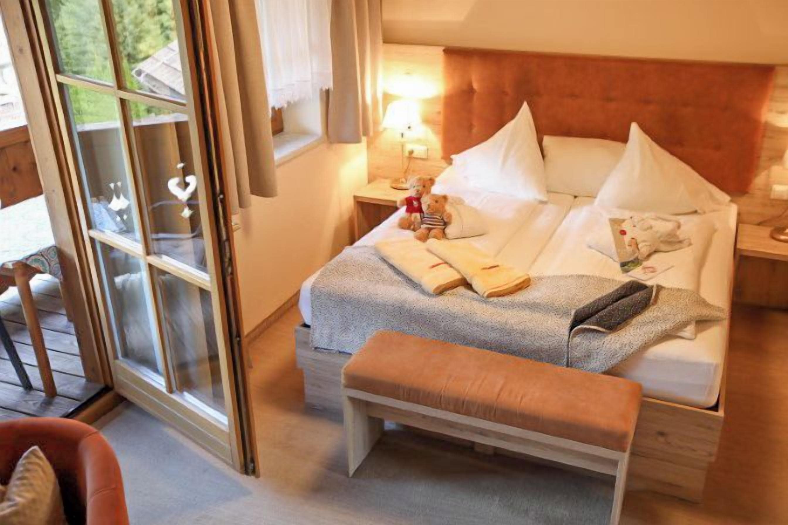 A bedroom with a bed, bedside table, lamp, and a bench.