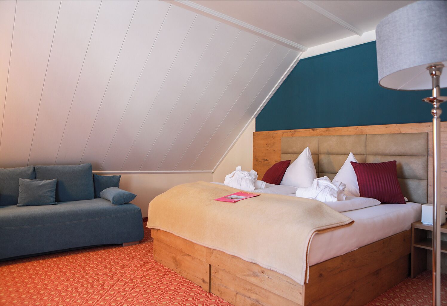 Un dormitorio con techo inclinado, una cama con muchos cojines, un sofá y una lámpara de pie.
