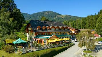 A large hotel with multiple floors, outdoor seating areas, and a view of the surrounding mountains.