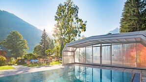 En swimmingpool med en glasvägg runt om, omgiven av träd och med ett berg i bakgrunden.