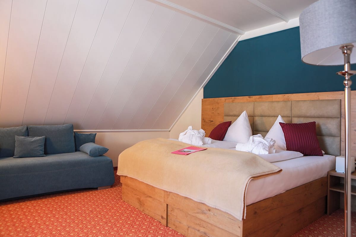 Une chambre avec un plafond en pente, un lit avec de nombreux oreillers, un canapé et une lampe sur pied.