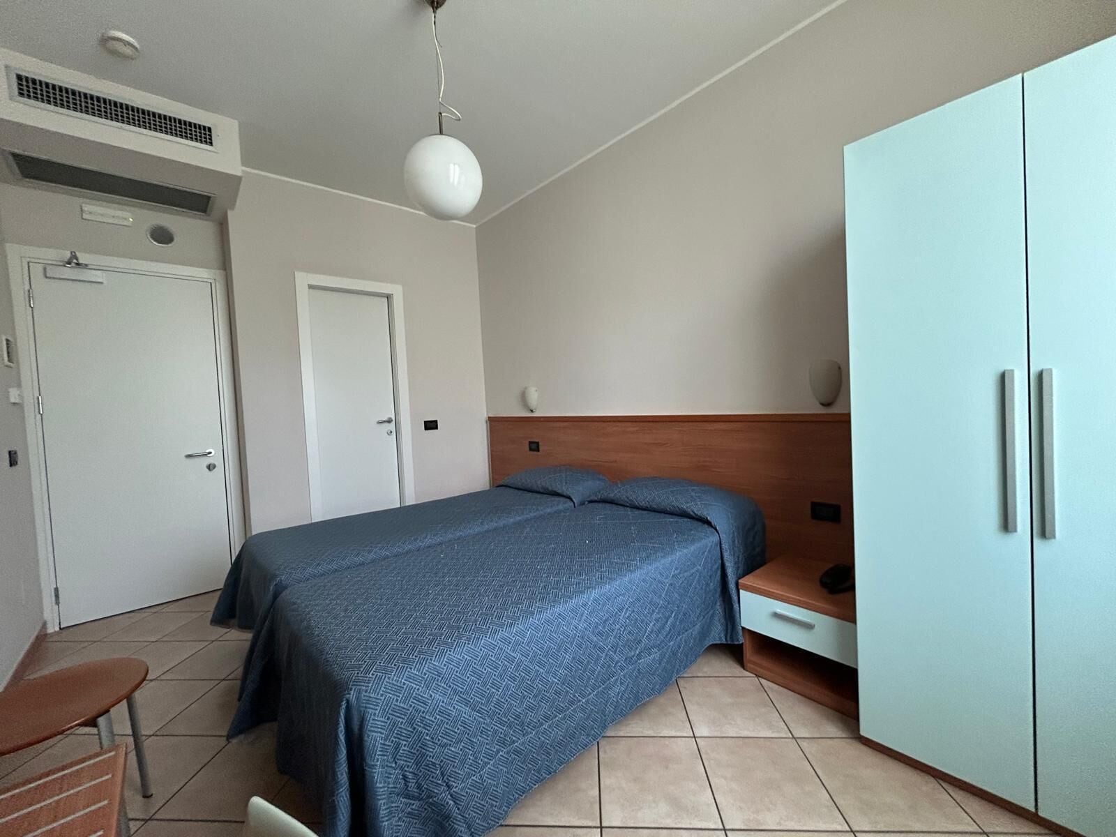 A bedroom with a bed, a wardrobe, a desk, and a chair.