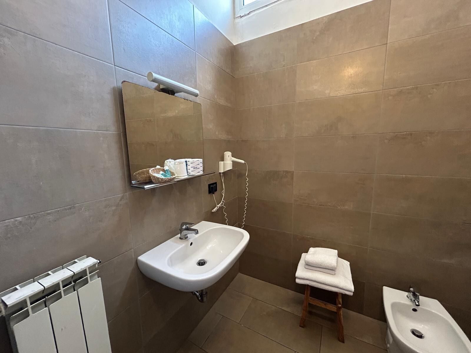 A bathroom with a white sink, a small wooden stool with a towel, and a bidet.