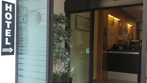 A hotel entrance with a reception desk, a potted plant, and a sign indicating the hotel's name. - Hotel Salerno (Milan)