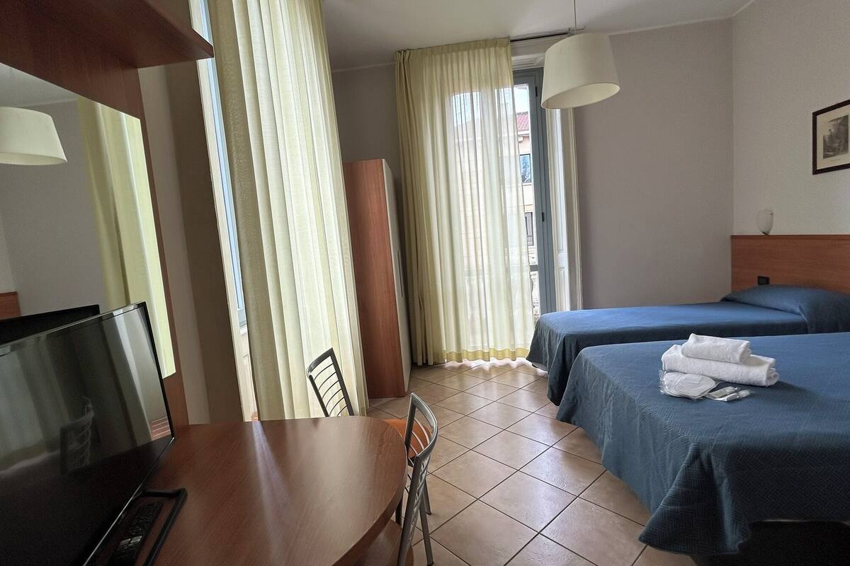 A hotel room with a TV, a desk, two beds, and a window with curtains.