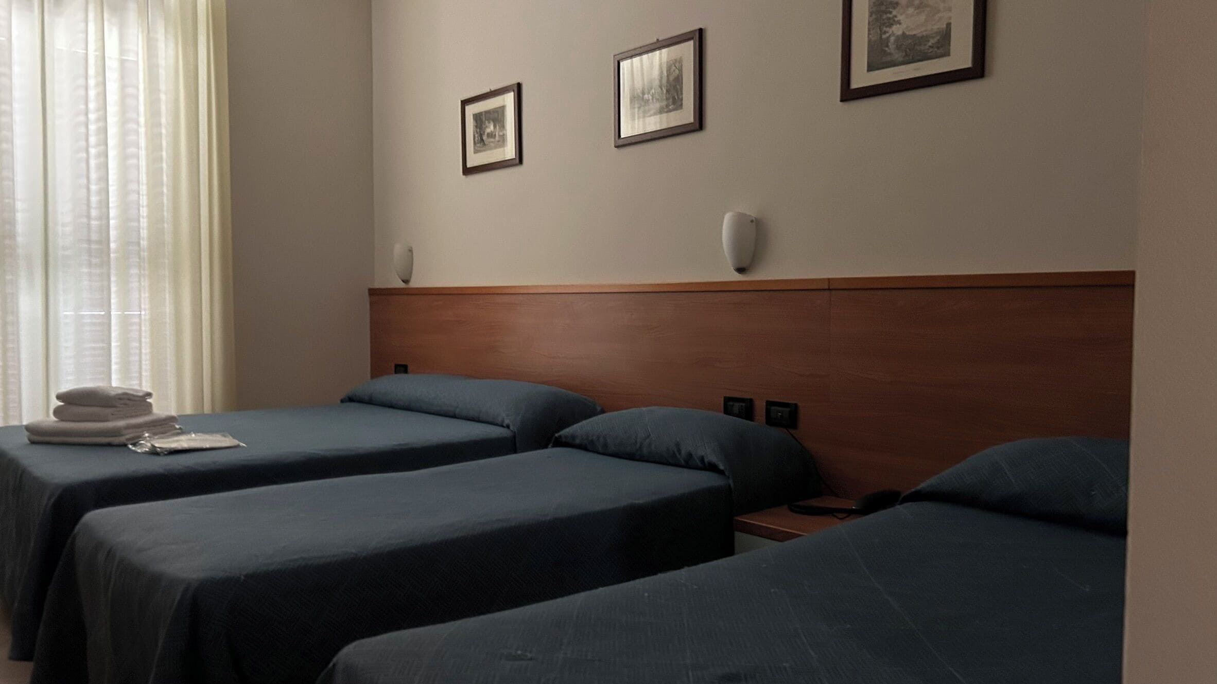 Quarto de hotel com duas camas de solteiro, uma mesa de cabeceira com abajur e três quadros na parede.