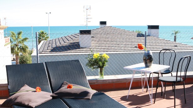 A rooftop terrace with a table and chairs, a lounge chair with a cushion, and a vase with flowers. - Hotel los Globos (Sitges)