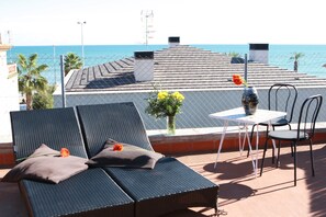 A rooftop terrace with a table and chairs, a lounge chair with a cushion, and a vase with flowers. - Hotel los Globos (Sitges)