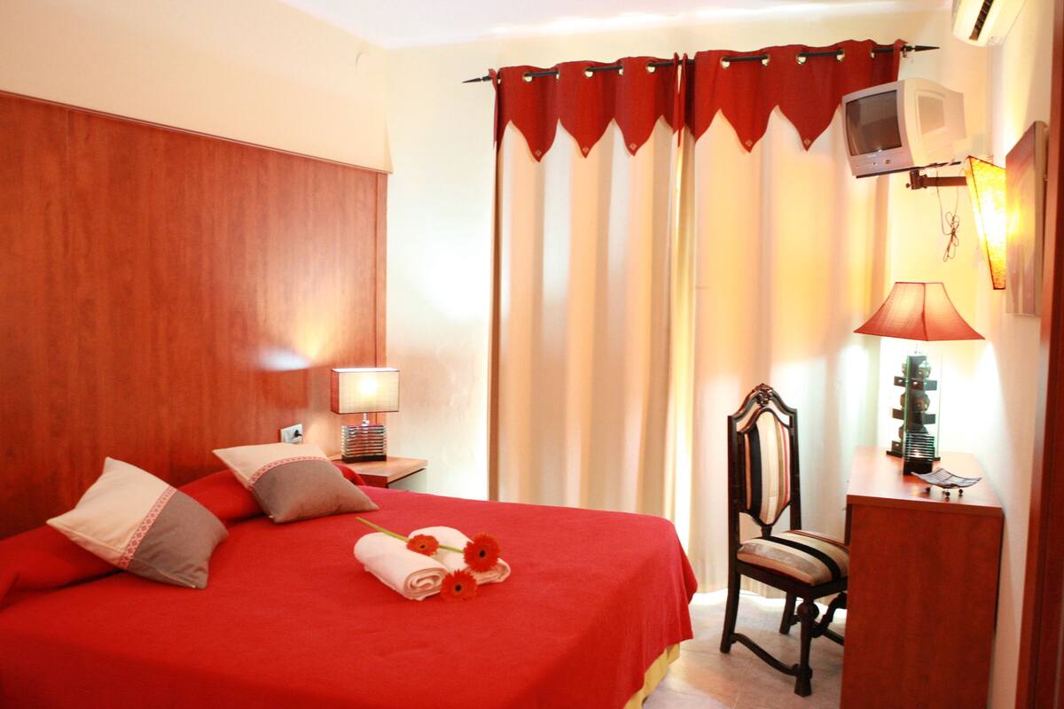 Una habitación de hotel con una cama, una silla, un escritorio, una lámpara y cortinas.