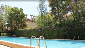 A swimming pool with metal railings, surrounded by lush greenery and trees. - Hotel los Globos (Sitges)