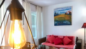 A living room with a sofa, a painting, a lamp, and a window with curtains. - Hotel los Globos (Sitges)