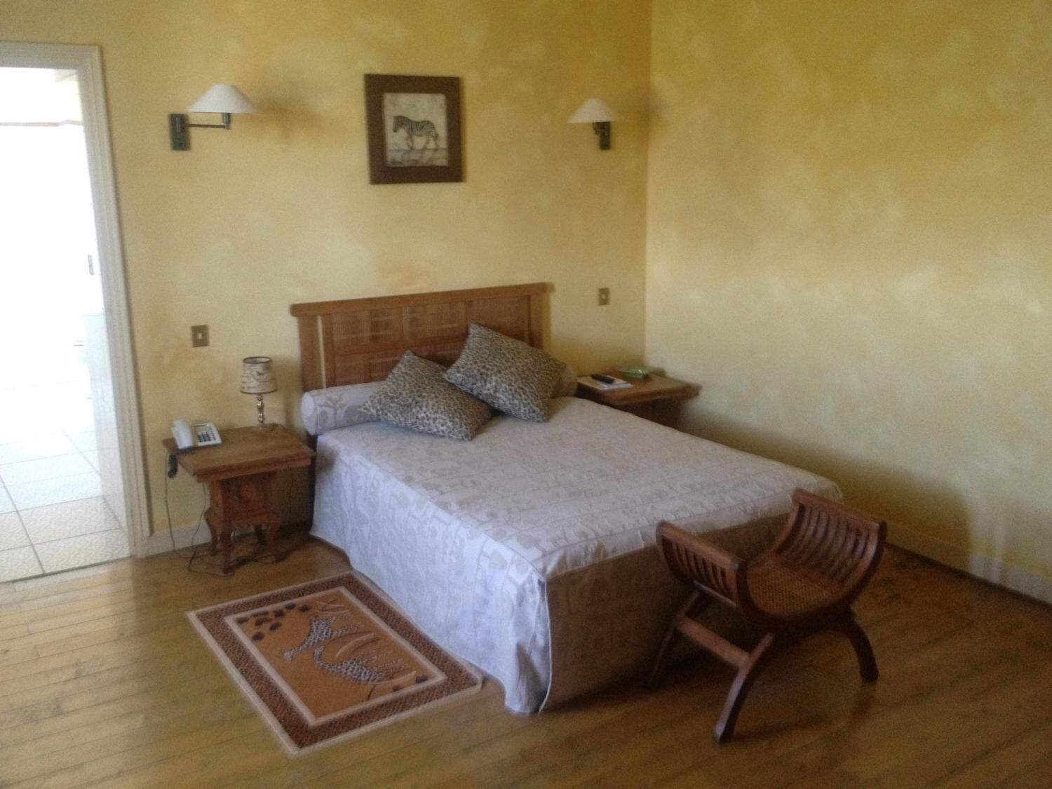 A bedroom with a wooden bed, two bedside lamps, a nightstand with a lamp, a chair, and a rug.
