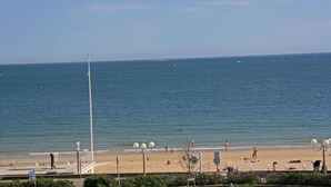 A beach with a clear view of the ocean, a few people walking, and a lifeguard tower.