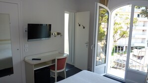 A hotel room with a bed, a desk, a chair, a TV, and a sliding glass door to the outside.