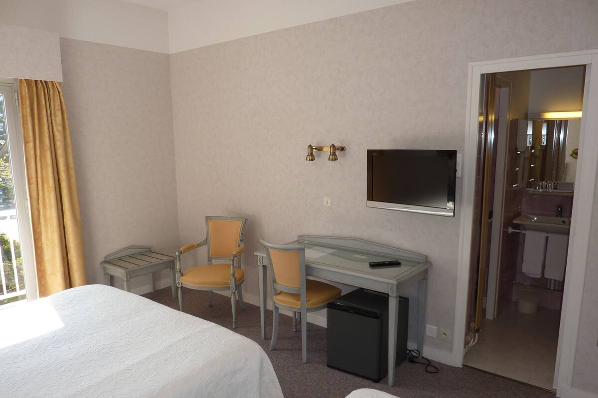 Una habitación de hotel con dos camas, un escritorio con una silla, un televisor y un refrigerador pequeño.