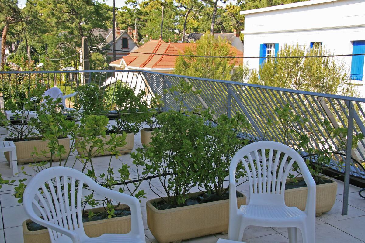 Un balcón con sillas de plástico blancas y plantas en macetas.