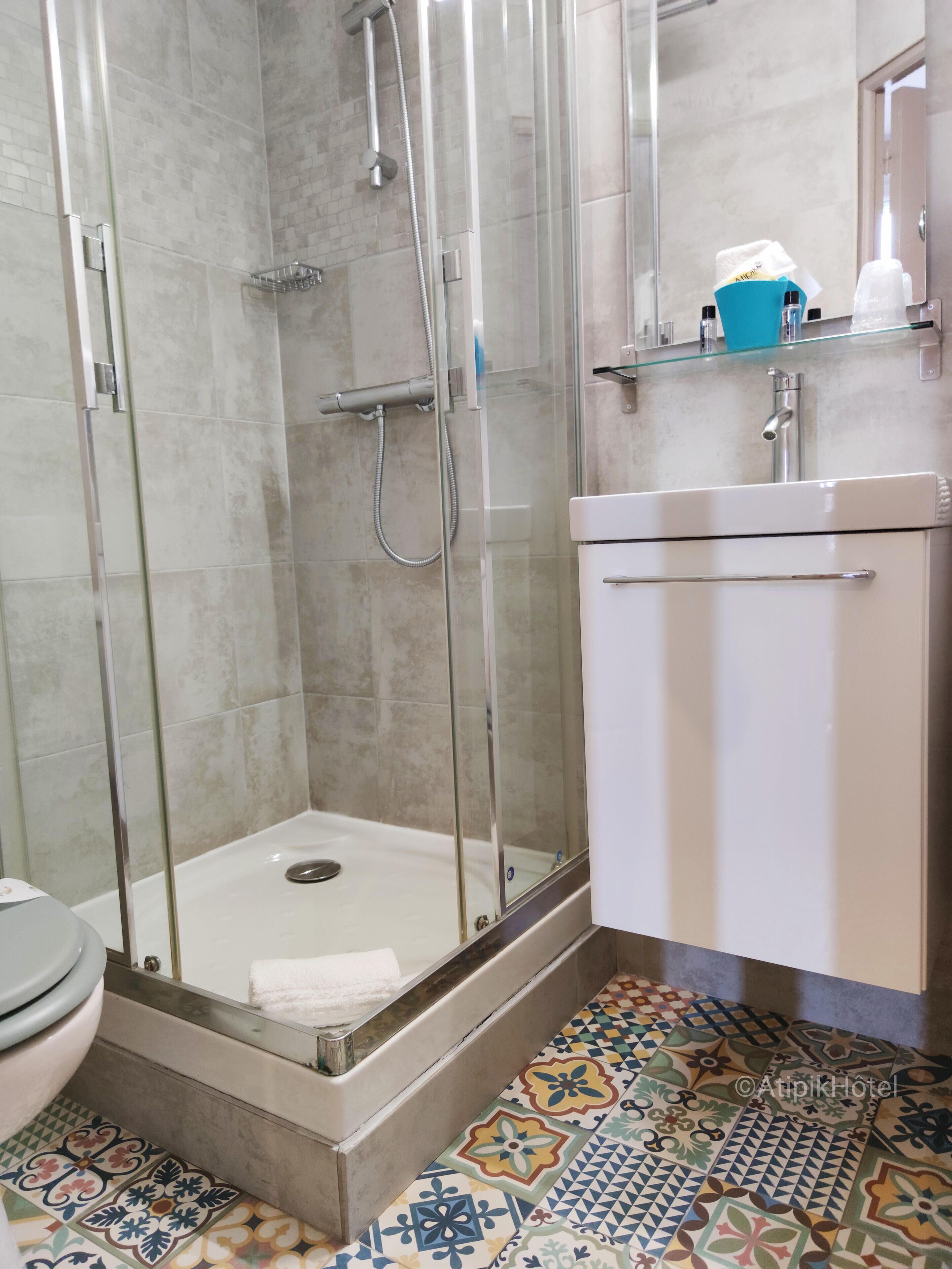 A shower area with a glass door, a white sink, and a tiled floor with a geometric pattern.