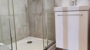 A shower area with a glass door, a white sink, and a tiled floor with a geometric pattern.