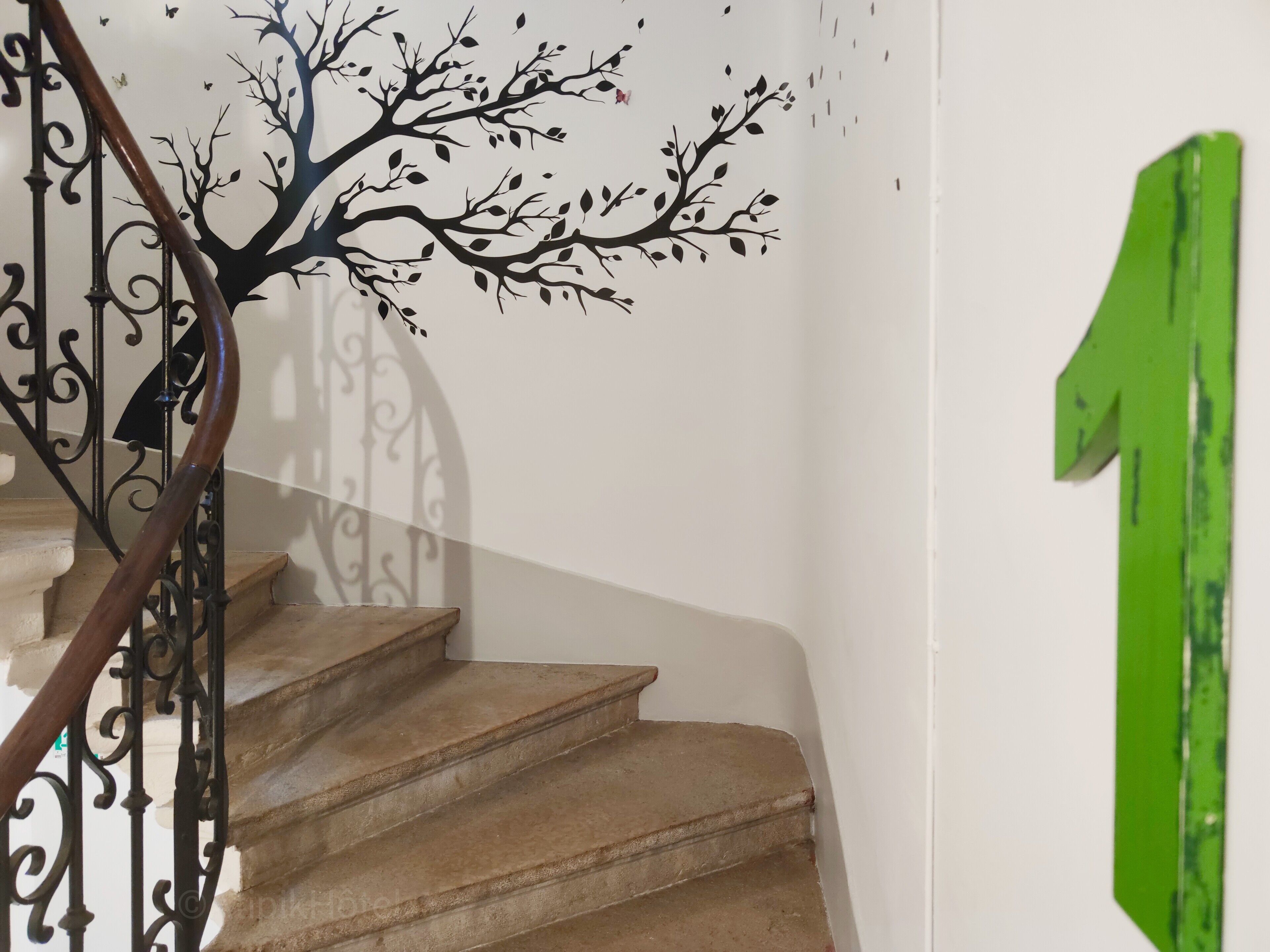 Una escalera con un adhesivo de árbol en la pared, una señal verde direccional y una barandilla de metal.