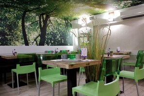 A restaurant with green chairs and tables, a mural of trees on the wall, and an air conditioning unit on the ceiling. - Atipik Hôtel (Annecy)