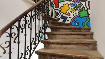 Una escalera con barandillas de metal negro decoradas y un mural colorido en la pared.