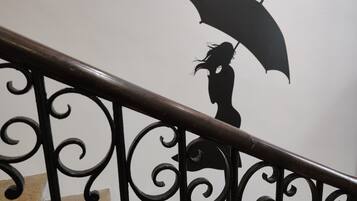 Una escalera con barandillas metálicas ornamentales y un mural en la pared de una mujer sosteniendo un paraguas.
