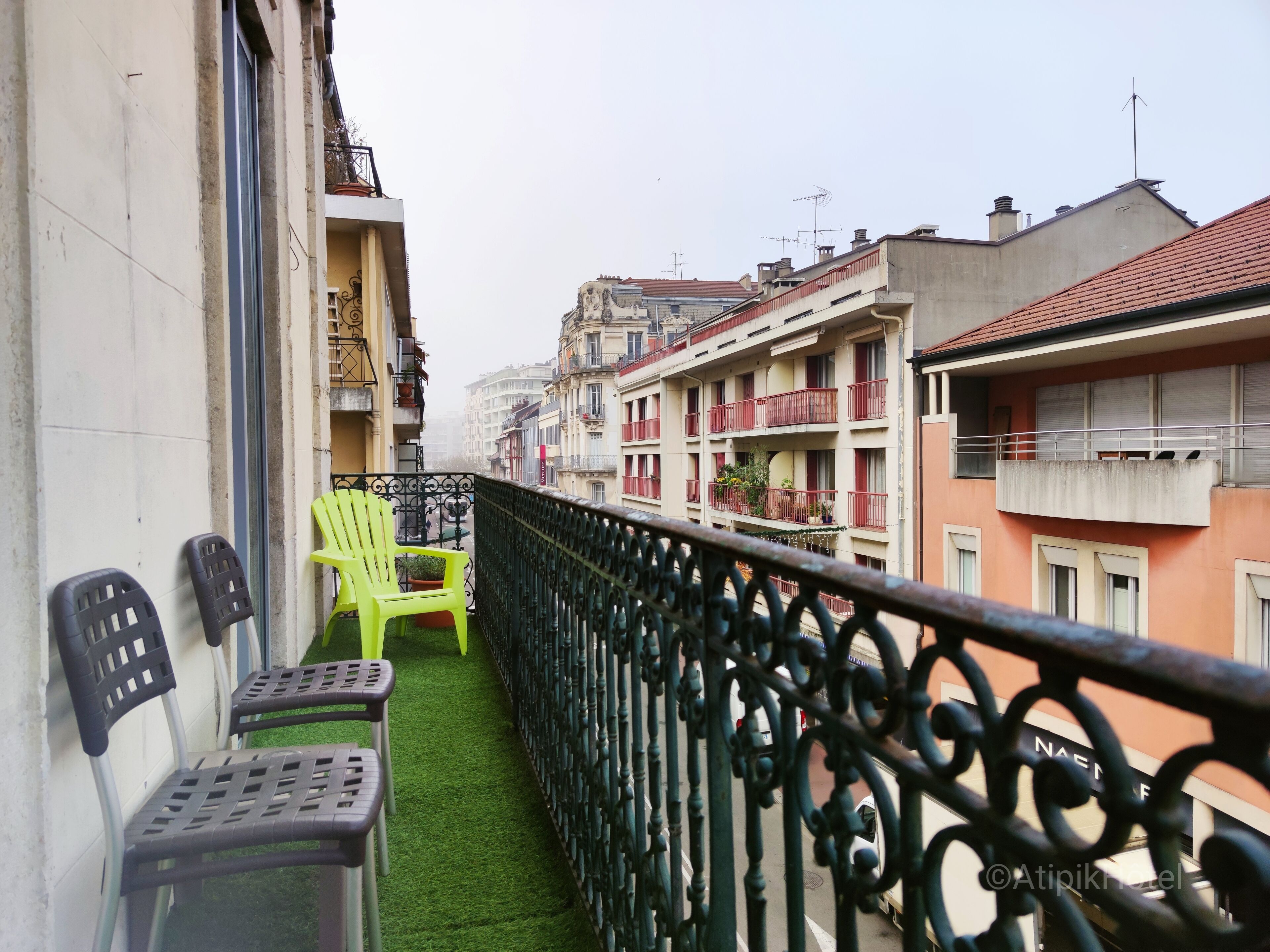A balcony with two plastic chairs and a small table, a green artificial grass floor, and a metal railing.