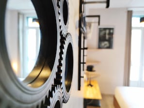 A close-up of a mechanical gear with a blurred background featuring a lamp and a bed. - Atipik Hôtel (Annecy)