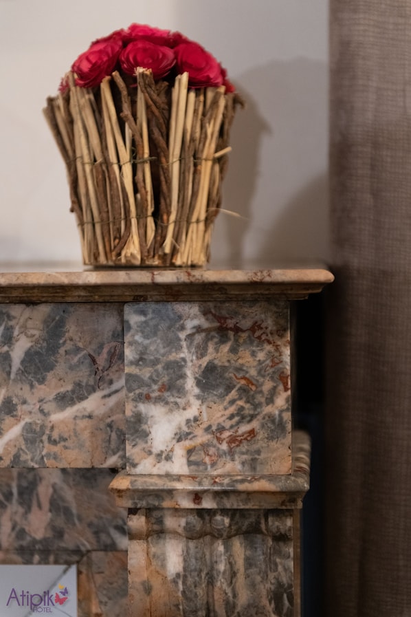 A marble fireplace with a woven basket of red flowers on top. - Atipik Hôtel (Annecy)