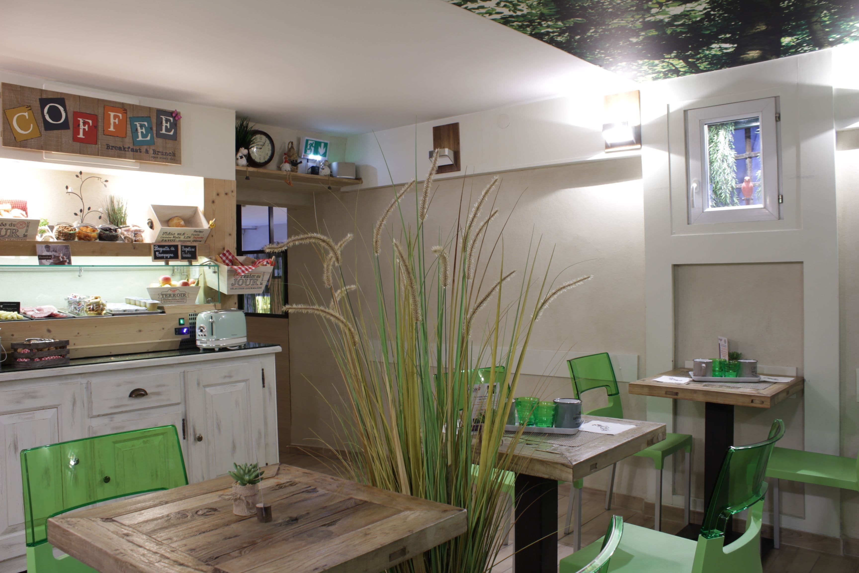 Un café acogedor con mesas de madera y sillas verdes, un letrero de café en la pared y un ventanal con vistas.