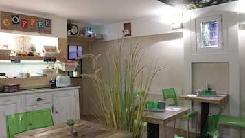 Un café acogedor con mesas de madera y sillas verdes, un letrero de café en la pared y un ventanal con vistas.