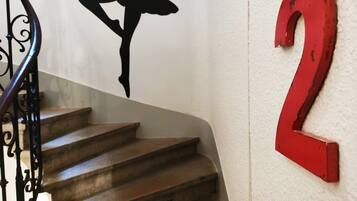 Una escalera con la silueta negra de un bailarín en la pared, un cartel con el número '2' en rojo y una frase francesa en los peldaños.