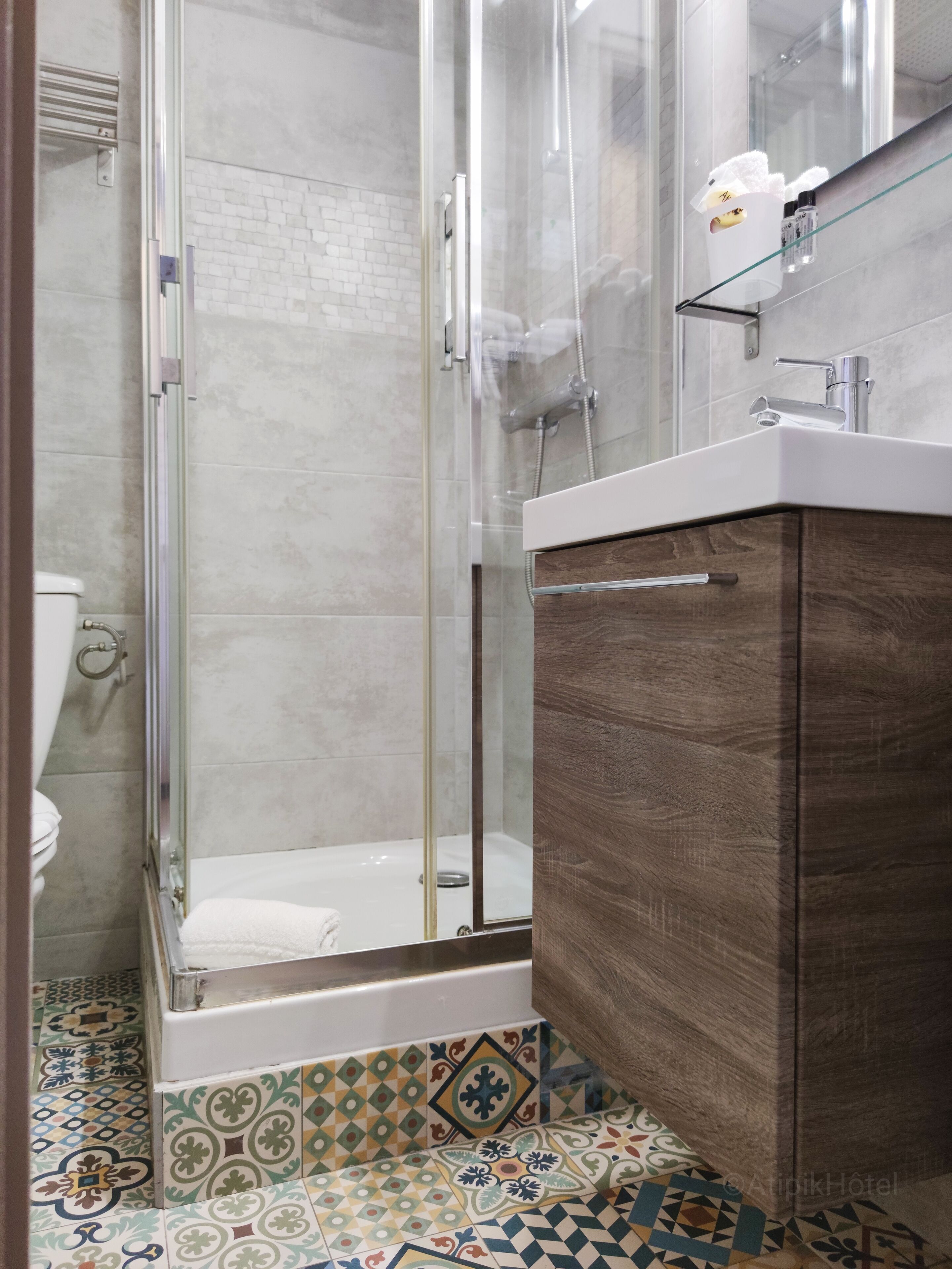 A modern bathroom with a glass-enclosed shower, a wooden vanity, and a tiled floor with a geometric pattern.