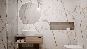 Ein modernes Badezimmer mit Marmorfliesenspiegel, einem runden Spiegel, einem Holzkosmetikschrank, einer freistehenden Badewanne und einer Toilette.