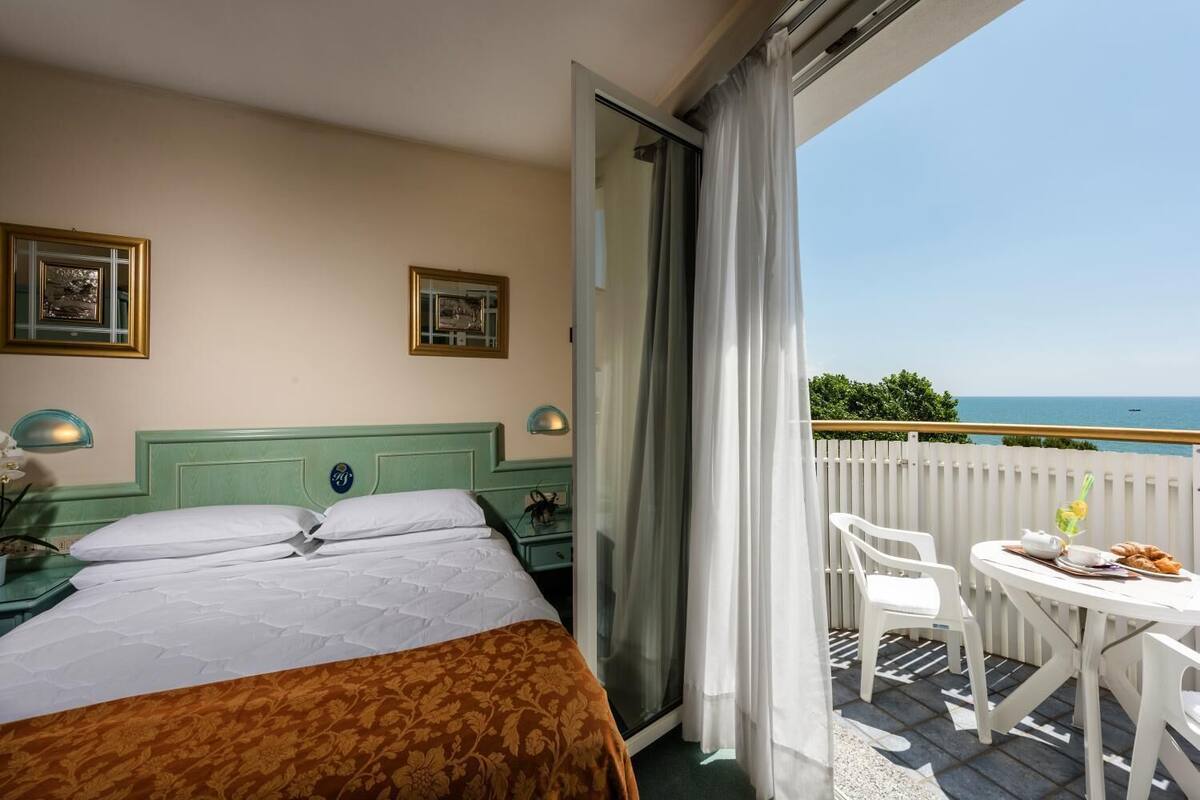 Una habitación de hotel con cama, un balcón con mesa y sillas, y vista al mar.