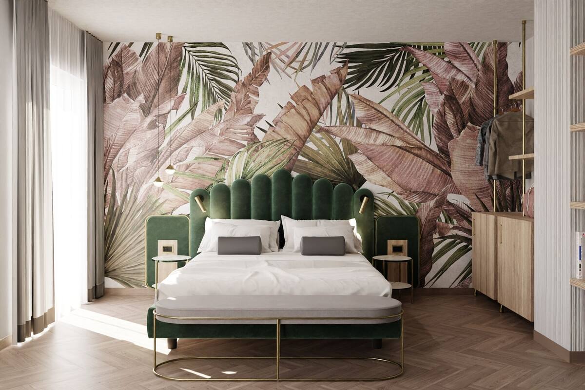 Un dormitorio con una cama tapizada en verde, ropa de cama blanca y un papel tapiz con estampado de hojas tropicales.
