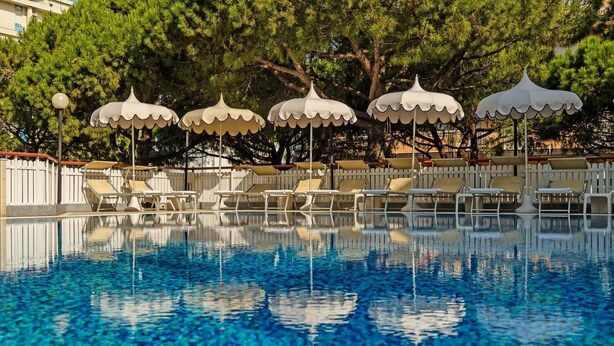 Ein Swimmingpool mit klarem, blauem Wasser, umgeben von weißen Sonnenschirmen und Liegestühlen.