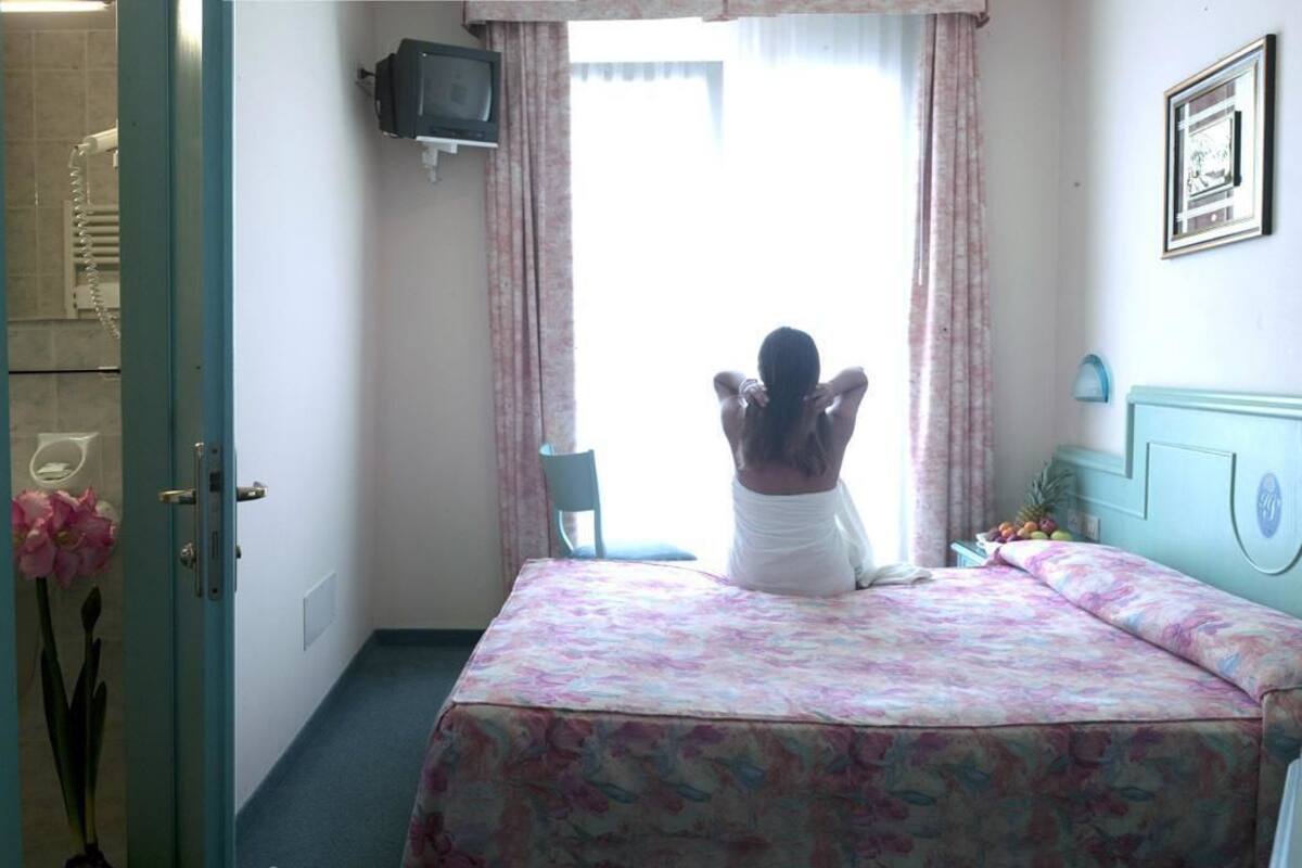 Un dormitorio con cama, televisor montado en la pared y ventana con cortinas.