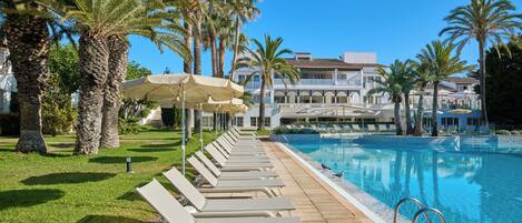 A poolside area with lounge chairs and umbrellas, palm trees, and a building in the background.