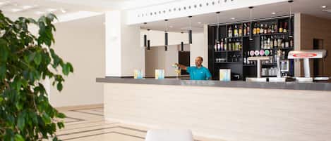 Un moderno vestíbulo de hotel con una recepción, un área de bar con varias botellas y una zona de estar con una mesa y sillas.