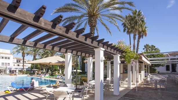 Ein Außenpoolbereich mit Liegestühlen und Sonnenschirmen, umgeben von Palmen und einer Pergola.