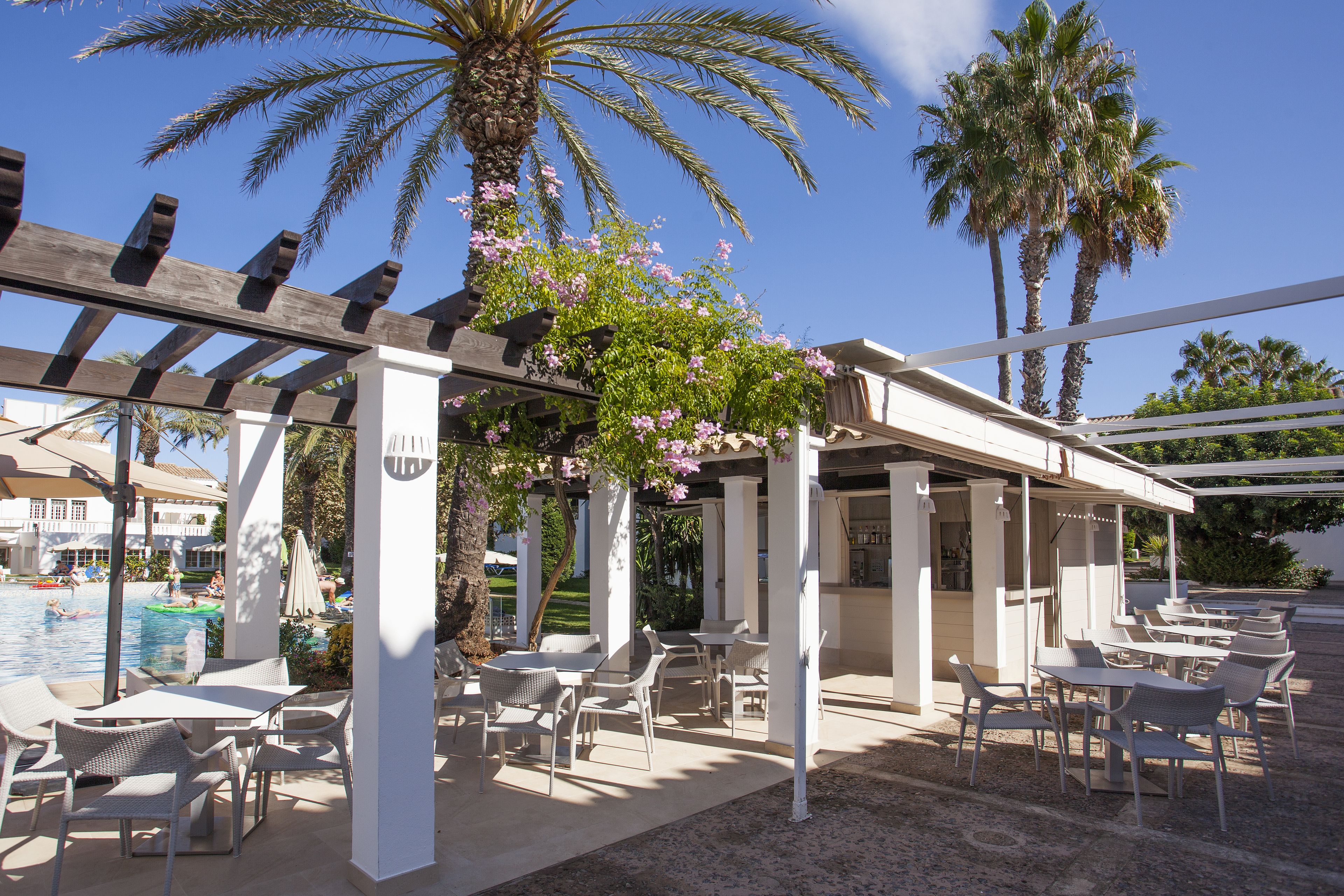 Un patio al aire libre con mesas y sillas, una piscina y palmeras.