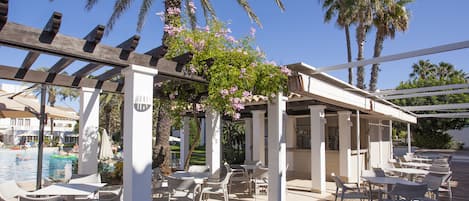 Un patio al aire libre con mesas y sillas, una piscina y palmeras.