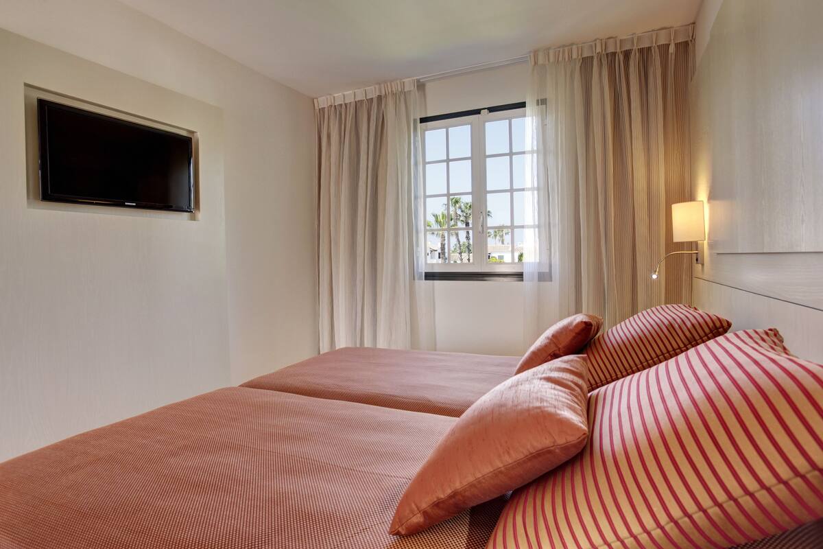Ein Hotelzimmer mit Bett, Vorhängen, einem Fenster und einem Flachbildfernseher.