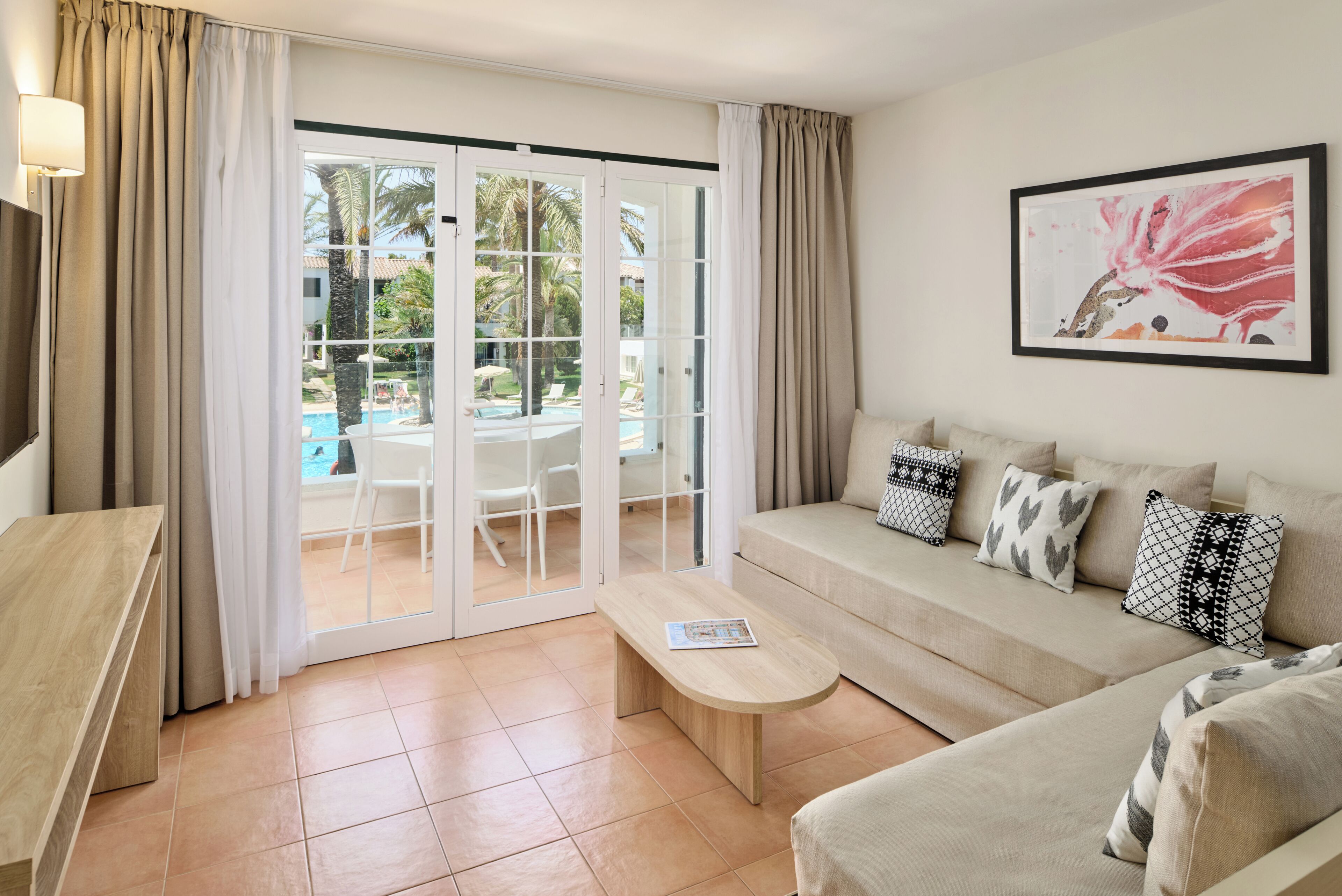 A modern living room with a sofa, a coffee table, and a view of a pool through a glass door.