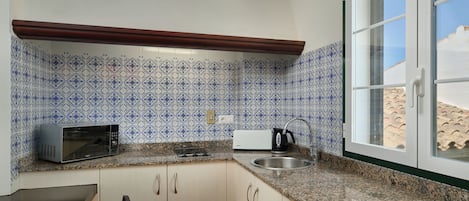A compact kitchen with a microwave, kettle, and sink.