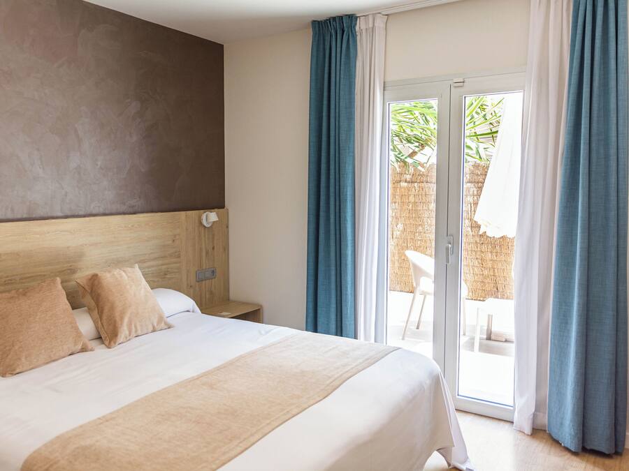 Habitación de hotel con una cama grande, cabecera de madera, mesita de noche y vistas a un espacio exterior con una mesa y sillas.