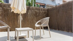 A patio area with a table and two chairs, a white umbrella, and a straw wall. - Hotel Bulevard (Benicassim)