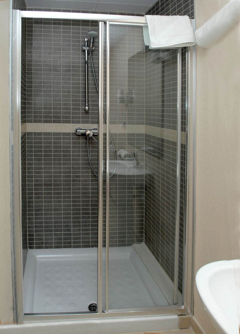 Una cabina de ducha con paredes de vidrio, un lavamanos blanco y una toalla colgada en la puerta.
